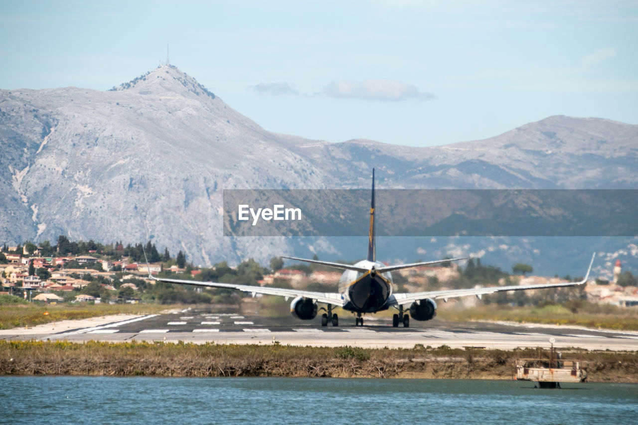 Airplane on sea by mountains against sky