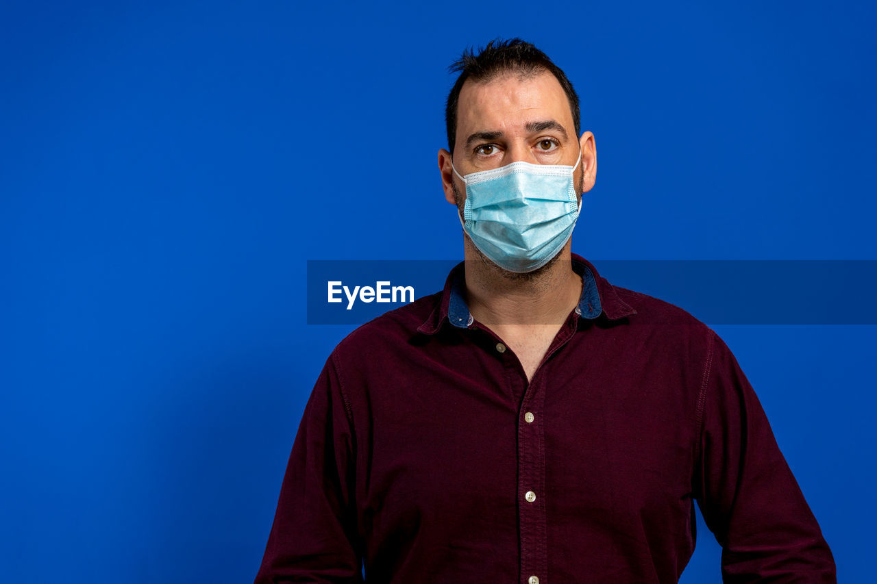 portrait, blue, one person, looking at camera, studio shot, adult, colored background, healthcare and medicine, front view, men, blue background, surgical mask, indoors, clothing, human face, person, occupation, protective mask - workwear, surgeon, young adult, glasses, copy space, doctor