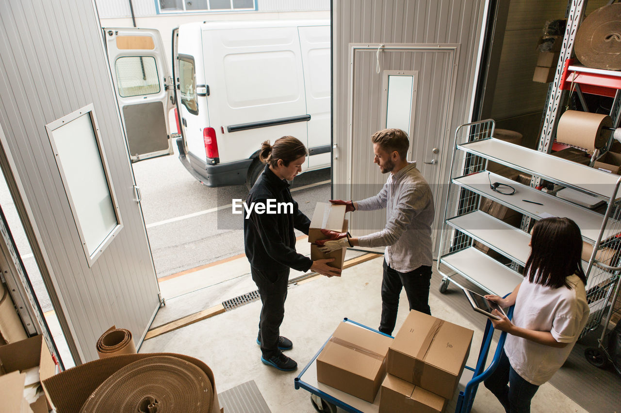 High angle view of male coworkers delivering boxes while female is using digital tablet