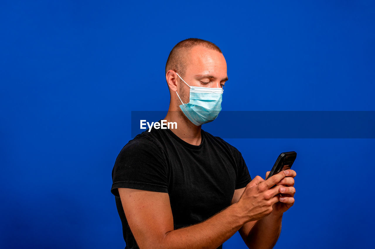 communication, blue, adult, men, one person, technology, wireless technology, mobile phone, studio shot, arm, portable information device, healthcare and medicine, smartphone, colored background, indoors, holding, blue background, person, activity, copy space, portrait, waist up, human face, hand, shaved head, telephone
