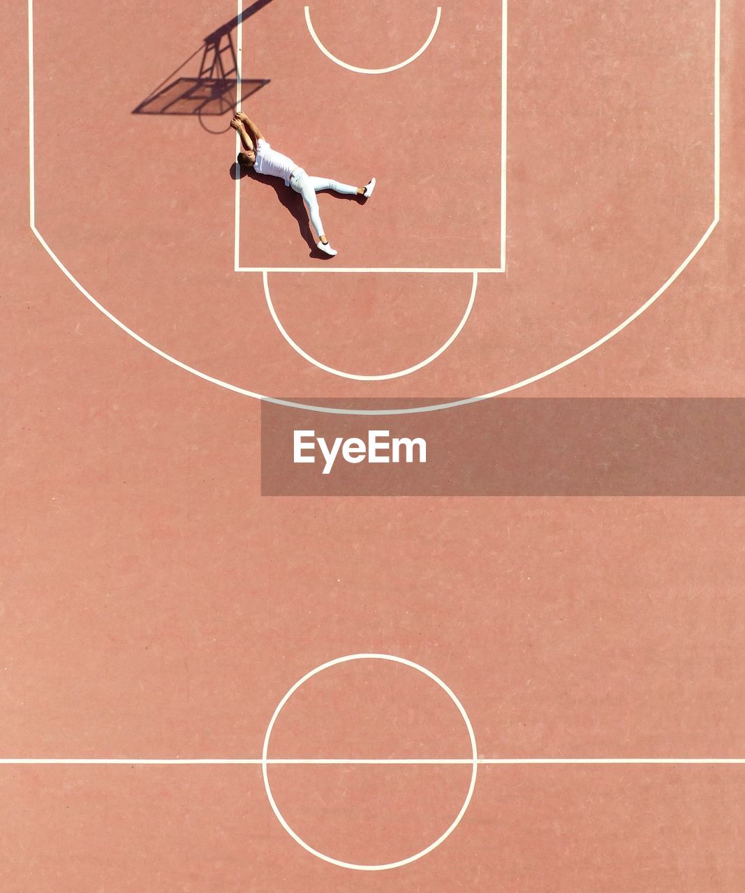High angle view of man lying on court by basketball hoop shadow