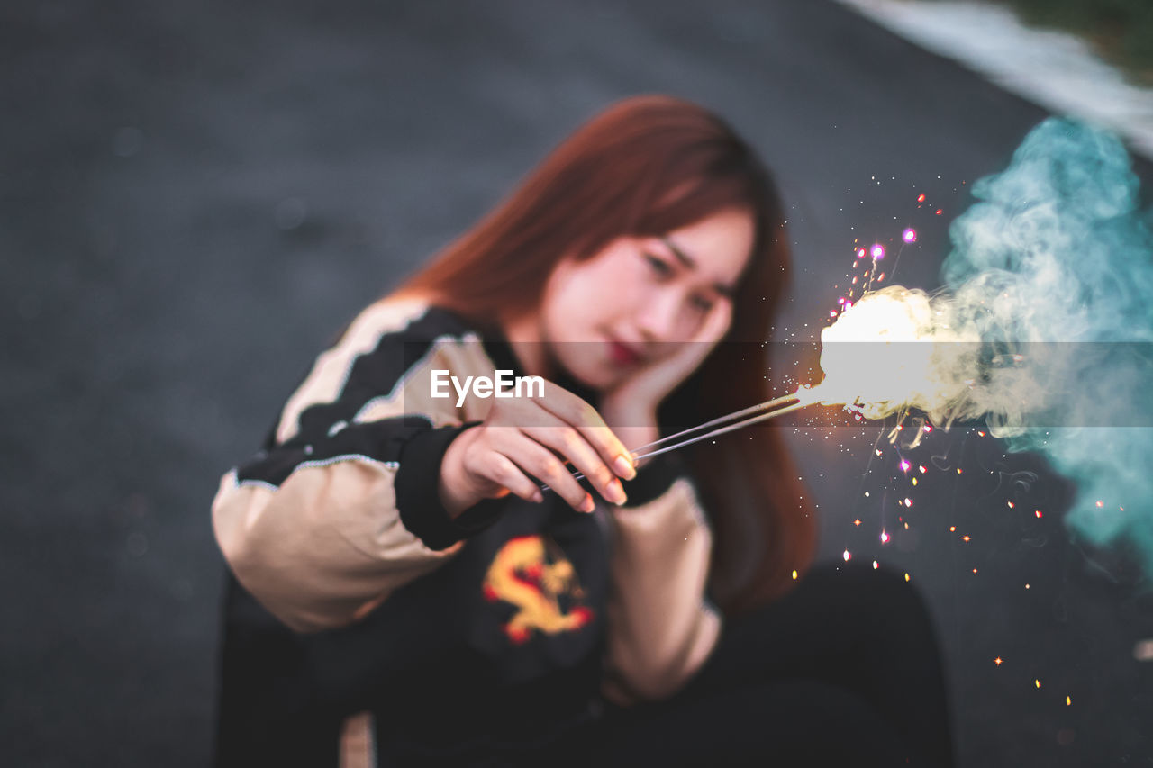 Young woman holding sparklers while sitting outdoors