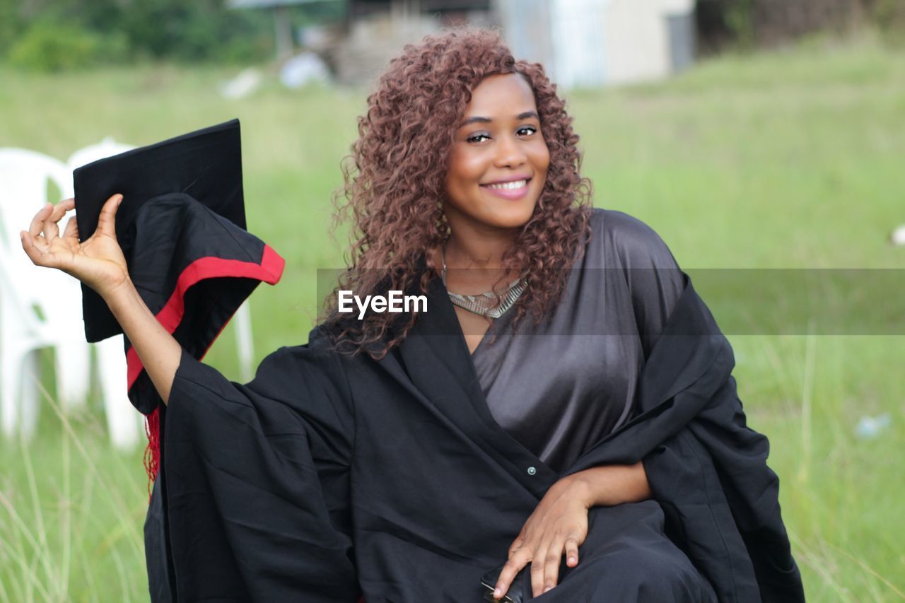 Portrait of smiling woman in graduation gown and mortarboard on field