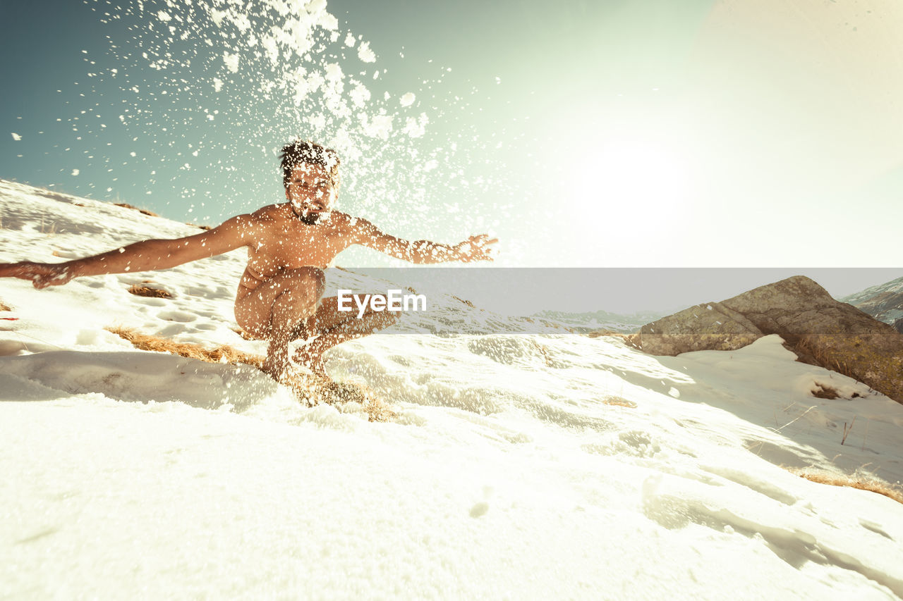 Low angle view of naked man throwing snow against sky