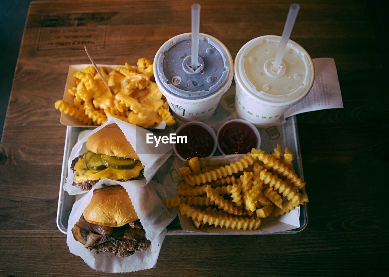 High angle view of drink by french fries and burgers on wooden table