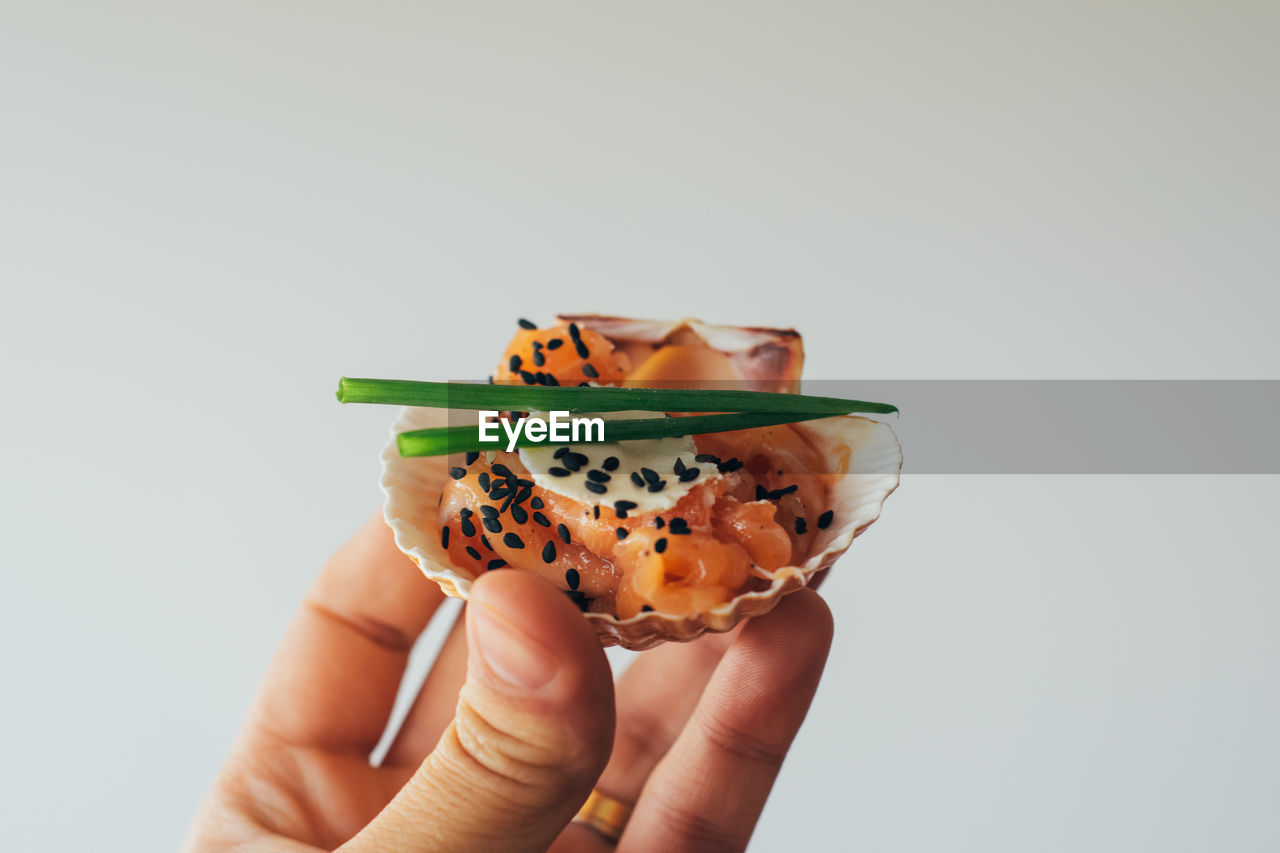 Cropped image of person holding cured salmon in seashell against white background