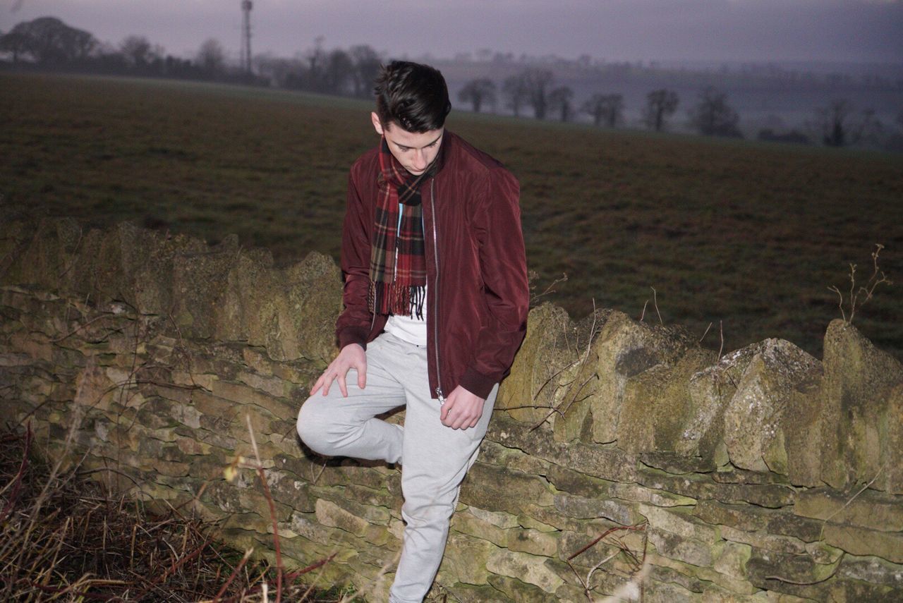 Young man standing against stone wall at dusk