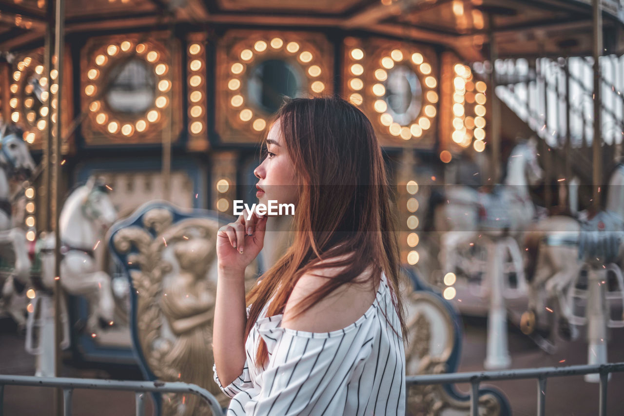 Woman looking away while standing by carousel