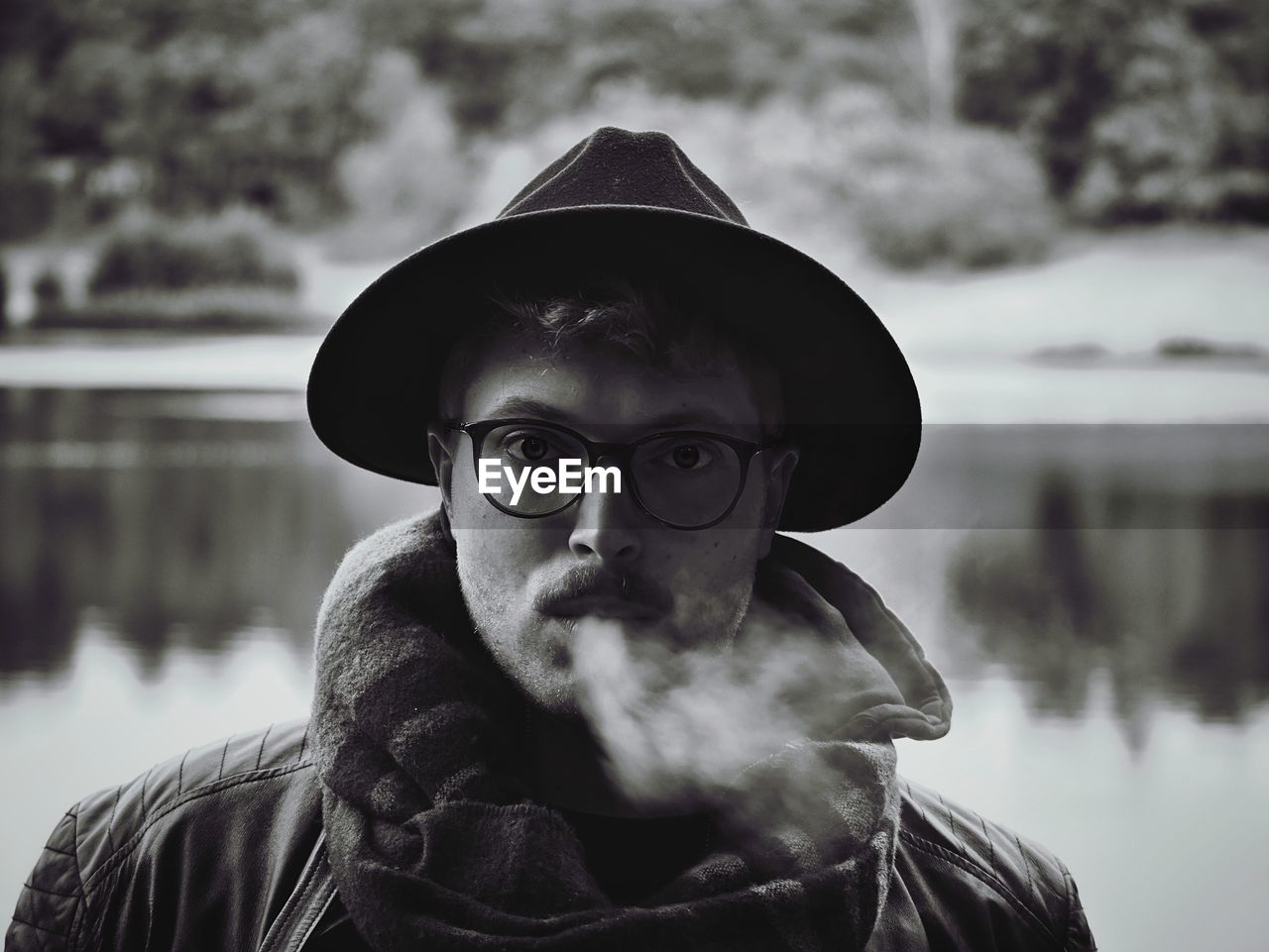 Portrait of man exhaling smoke against lake