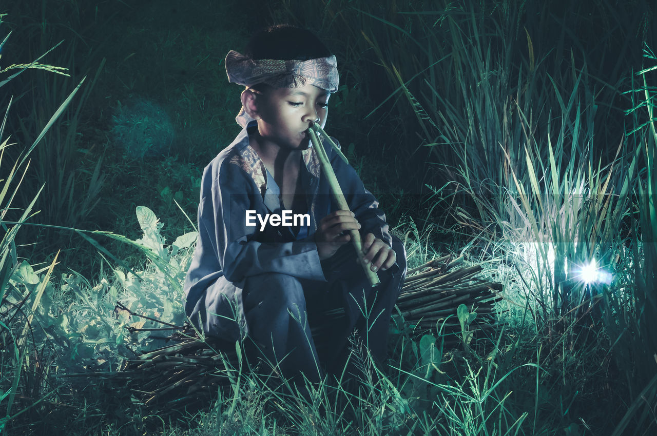 Boy playing flute on field at night