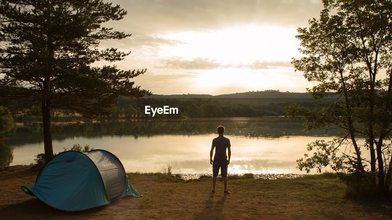 Rear view of man looking at lake while standing by tent