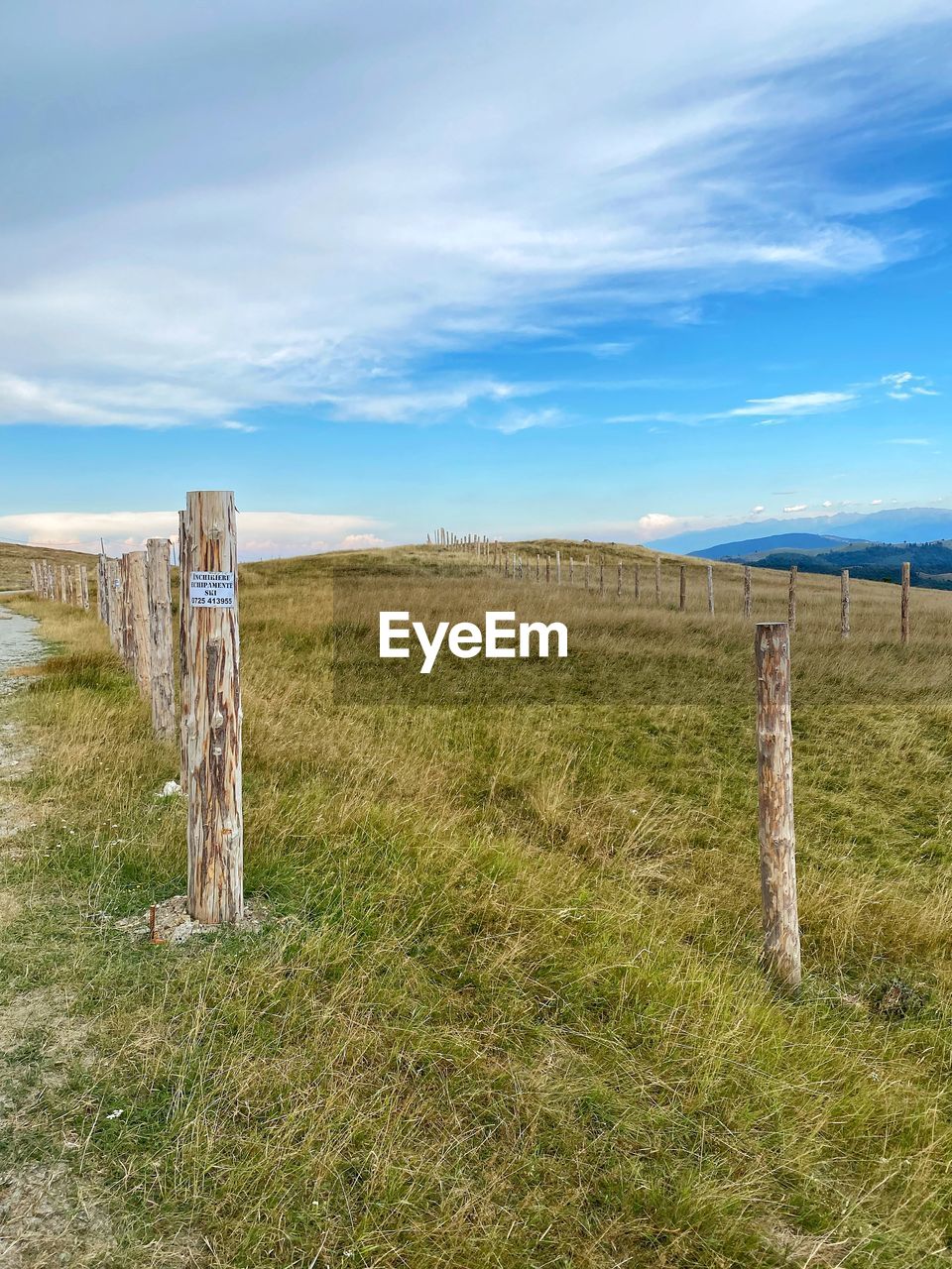WOODEN FENCE ON FIELD BY ROAD AGAINST SKY