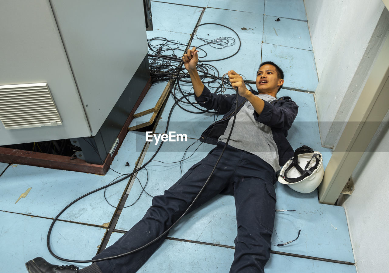 Shocked man holding cables while lying on floor by fuse box