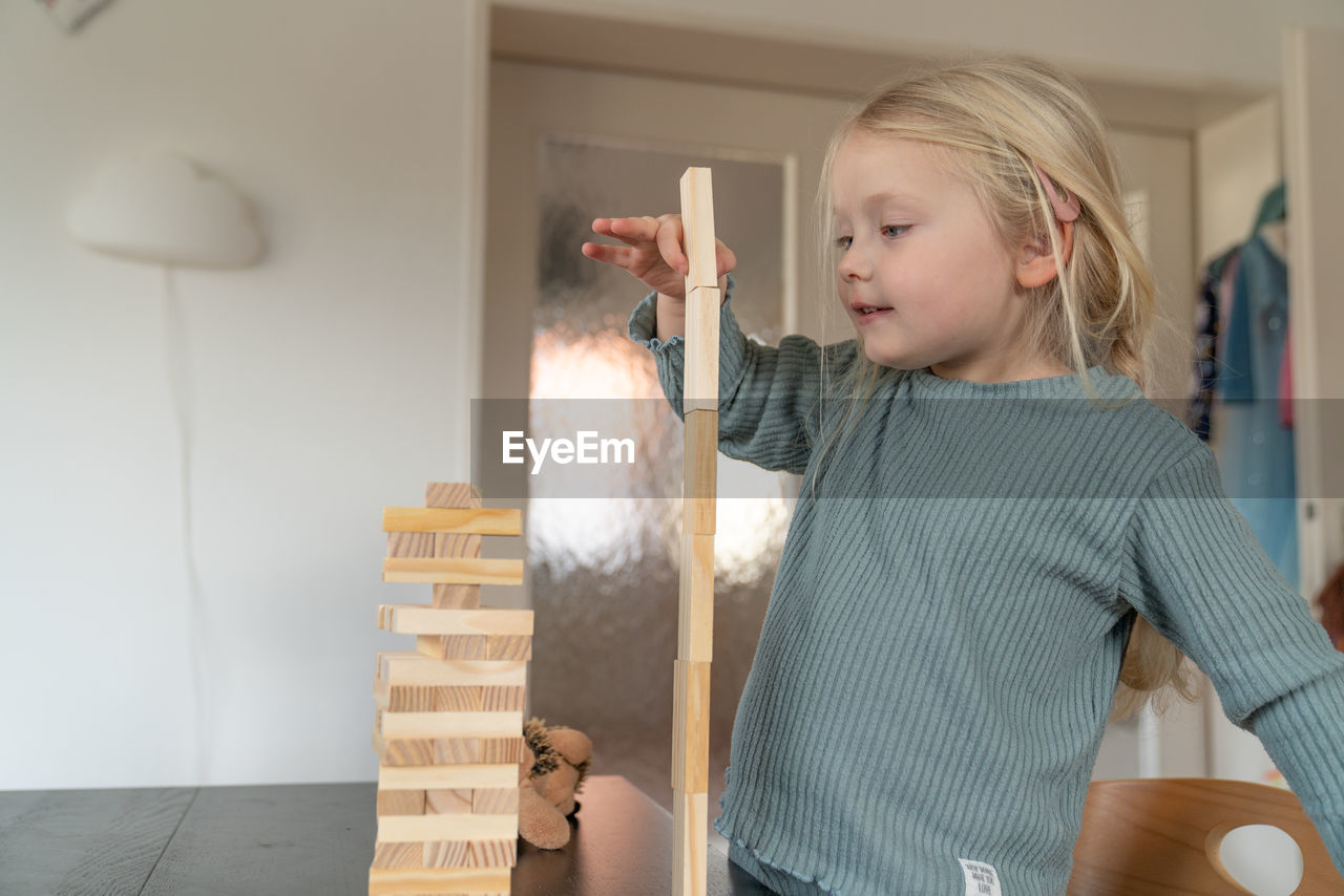 A toddler girl builds a wooden tower on a table