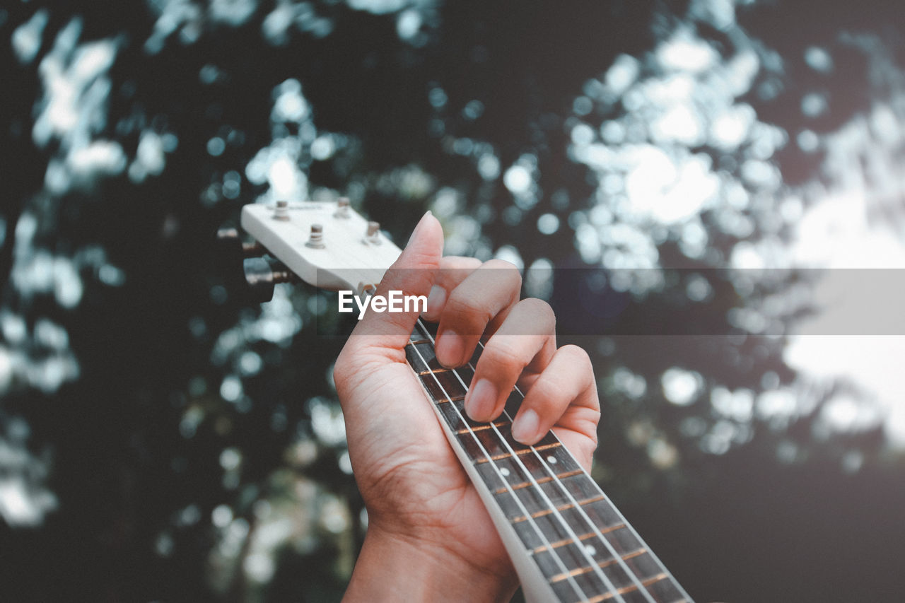 Close-up of hand playing guitar against tree