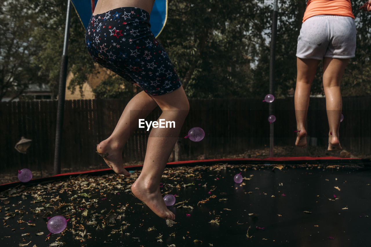 Low section of sisters jumping on trampoline against trees at park