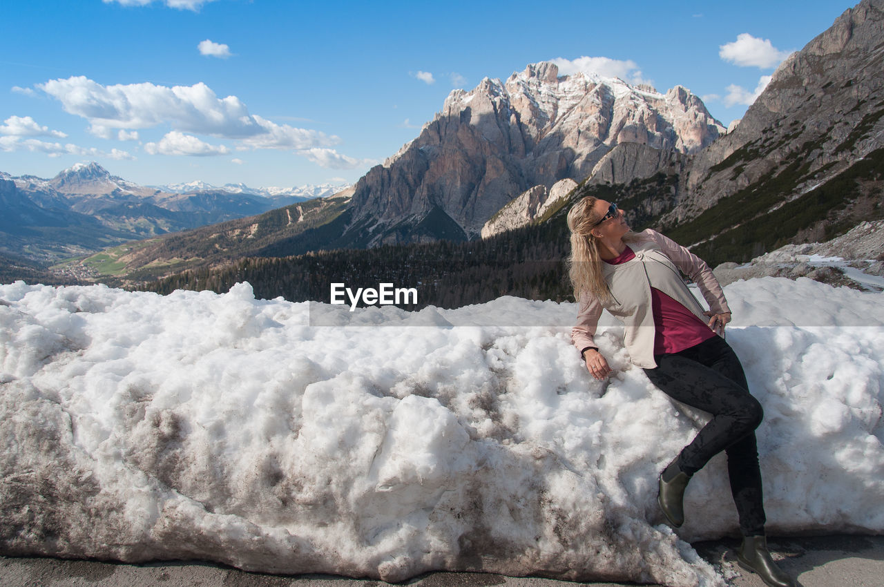FULL LENGTH OF WOMAN STANDING ON SNOWCAPPED MOUNTAIN AGAINST SKY