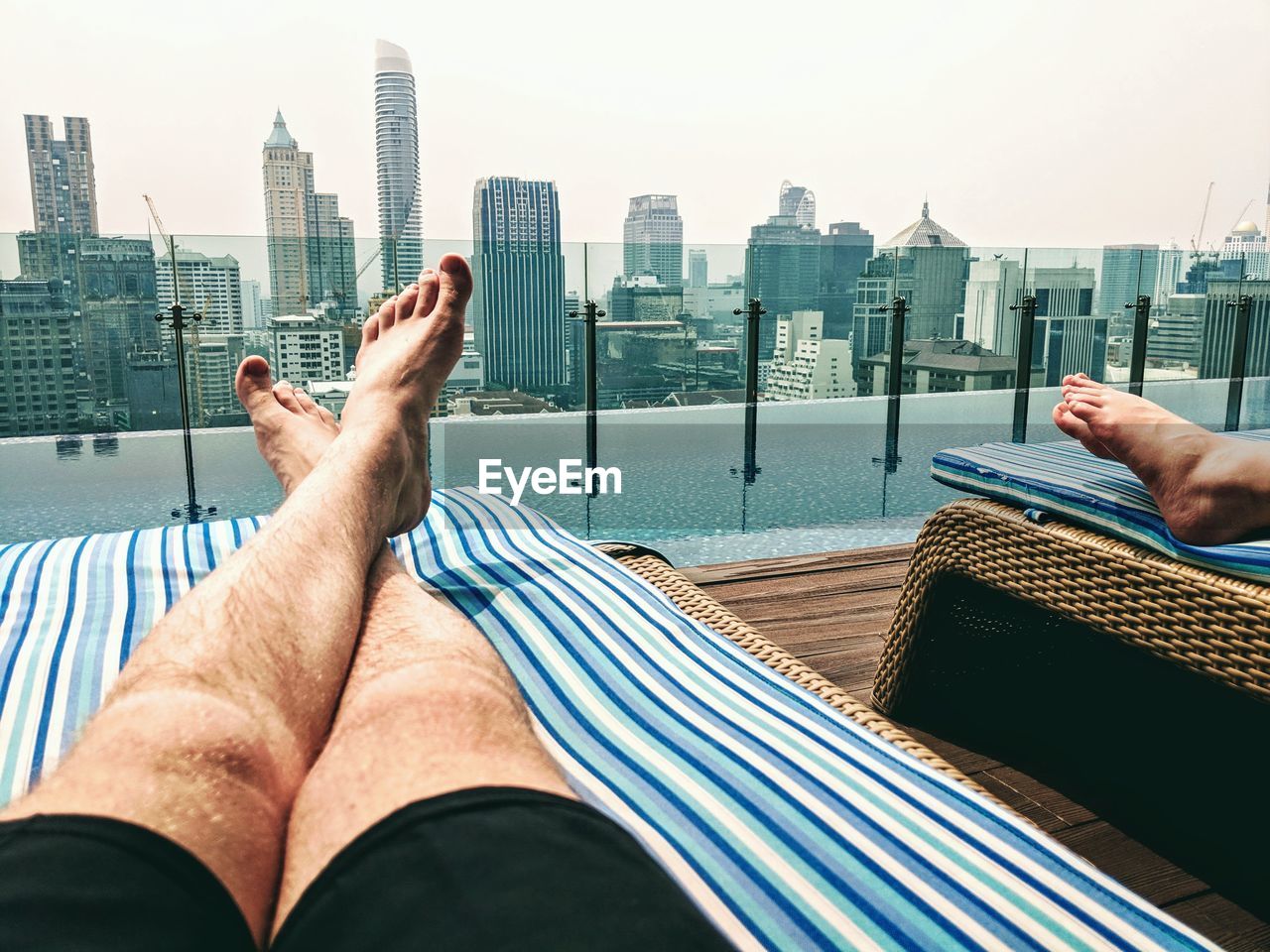 Low angle view of man relaxing at poolside against modern buildings