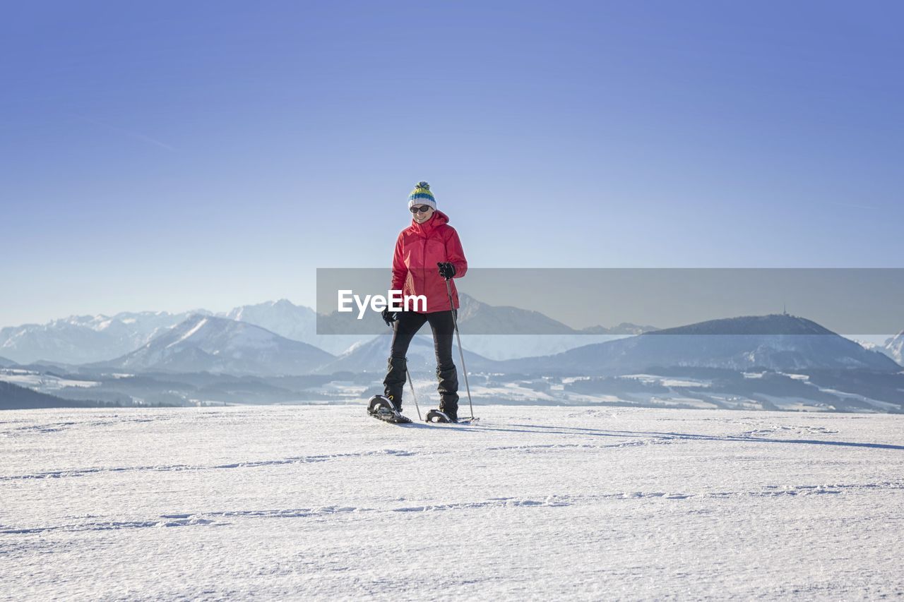 Woman snowboarding on land against clear blue sky