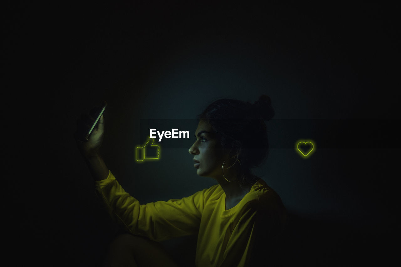 Profile view of woman using phone with icons in darkroom