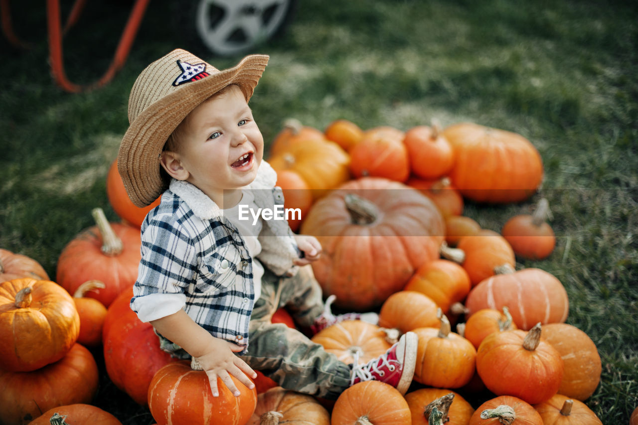 A laughing kid in a cowboy hat sits on bright orange pumpkins. holiday, halloween