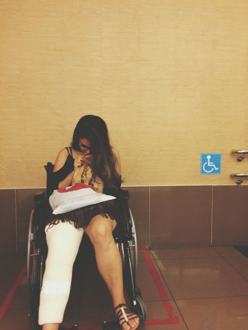 Young woman with broken leg sitting on wheelchair at hospital