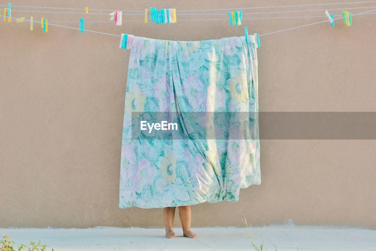Young child hanging floral bedsheet to dry outside