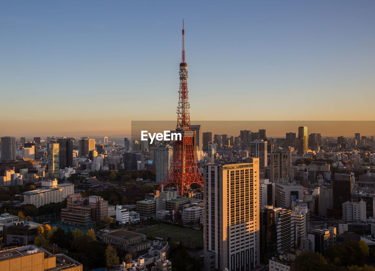 Tokyo tower amidst buildings in city against clear sky during sunset