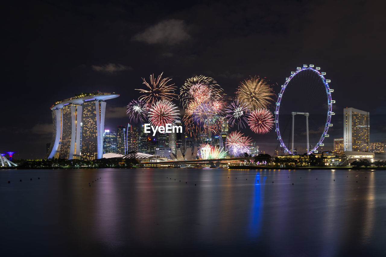 Firework display over illuminated city against sky at night