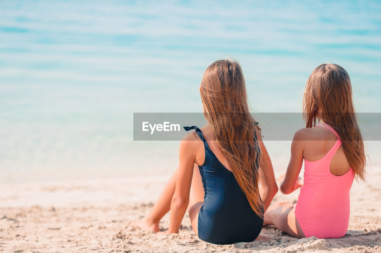 Rear view of sisters sitting on beach