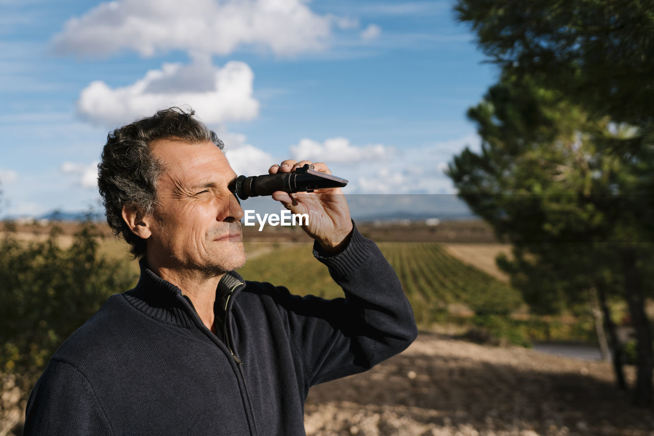 Winemaker looking through refractometer at vineyard