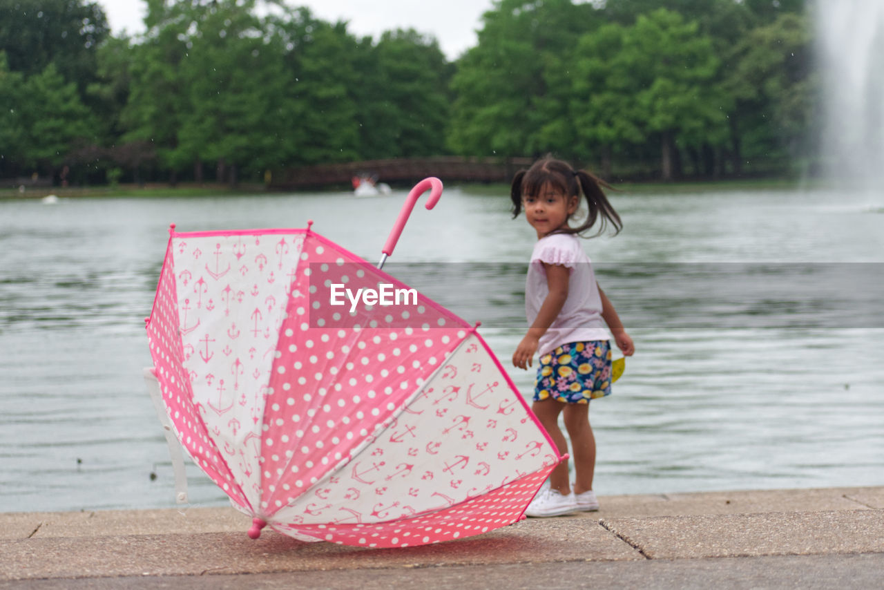 Full length of cute girl with pink umbrella on water