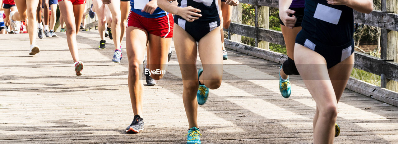 Girls running in a cross country race at sunken meadow state park crossing a wood bridge.