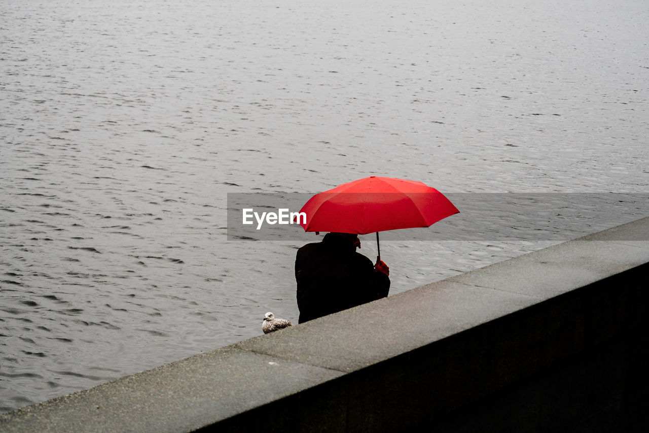High angle view of man with red umbrella by retaining wall against lake