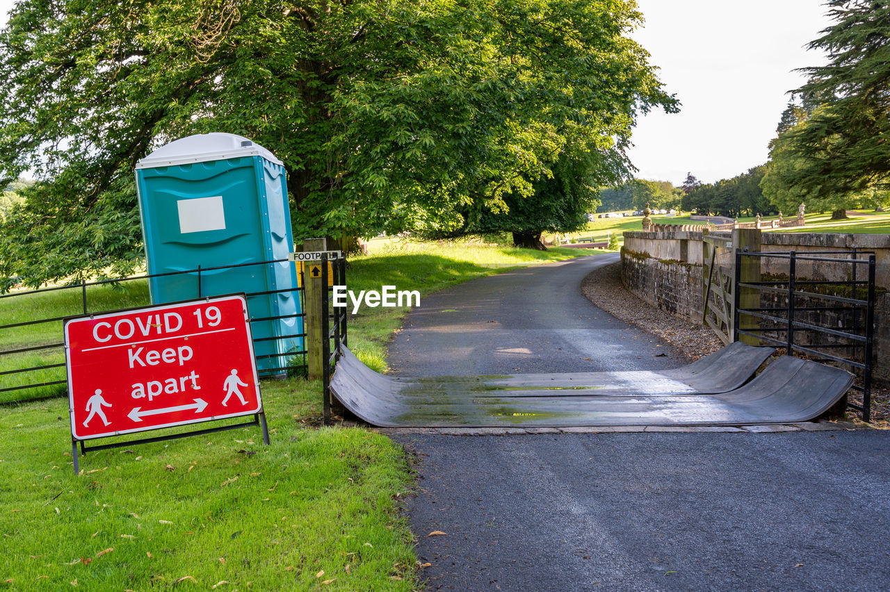 Covid-19 social distancing warning sign and portable toilet on public footpath at outdoor event