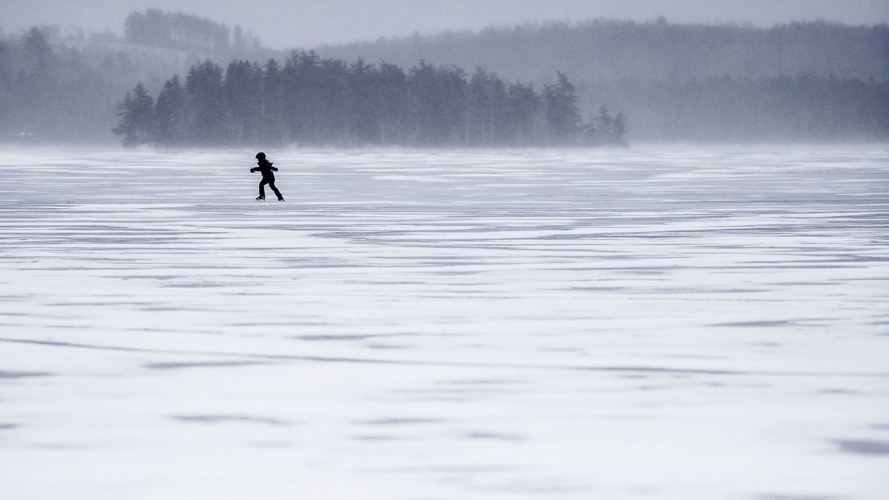 Distant view of silhouette boy ice skating on frozen lake