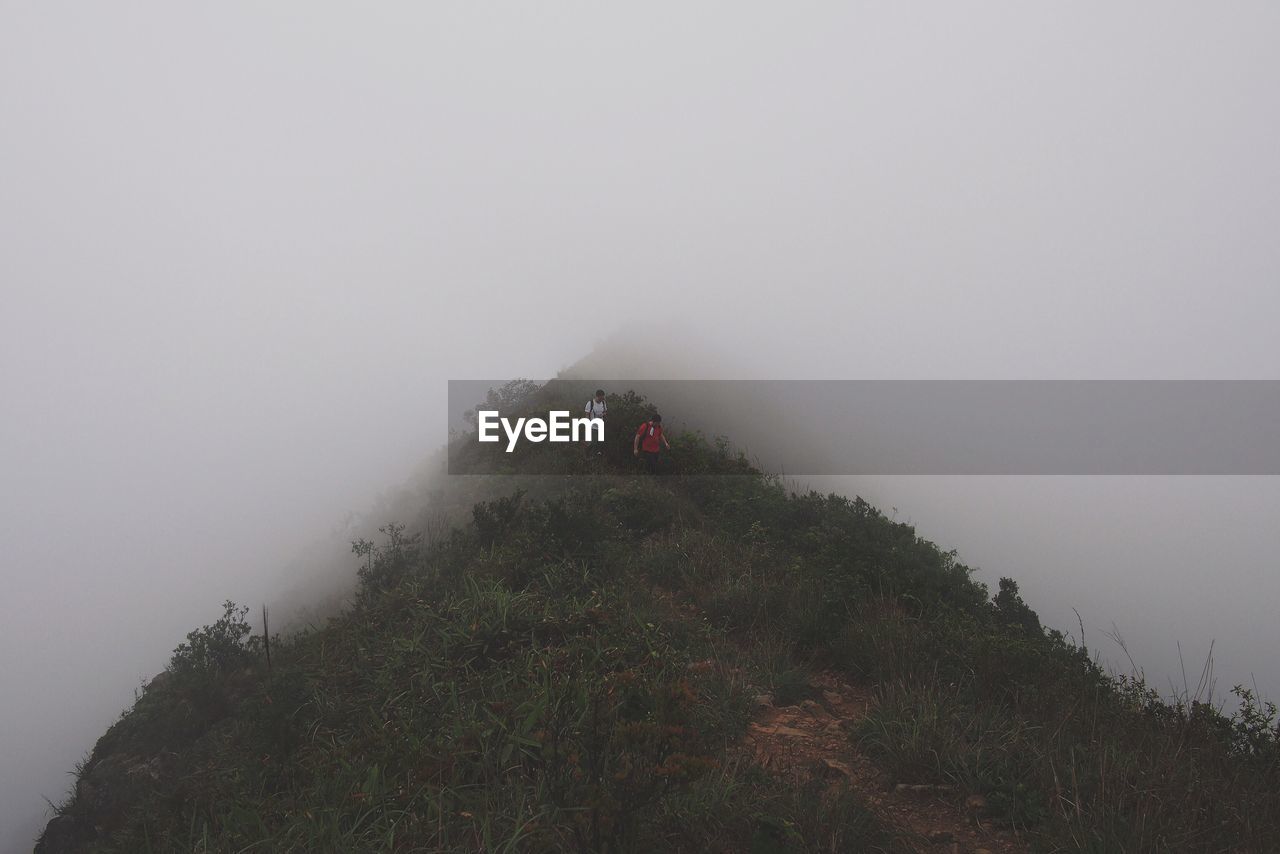Low angle view of people on mountain against sky during foggy weather