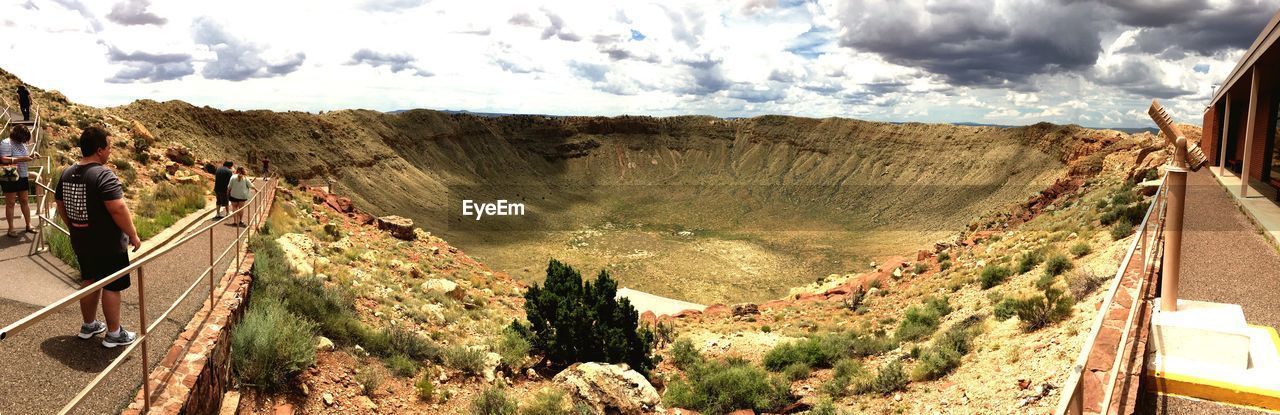 Panoramic view of people on walkway in volcanic crater against sky