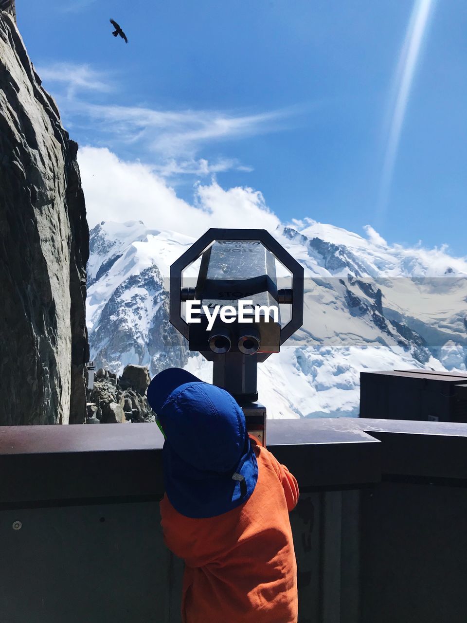 Rear view of boy looking through coin-operated binoculars against snowcapped mountains