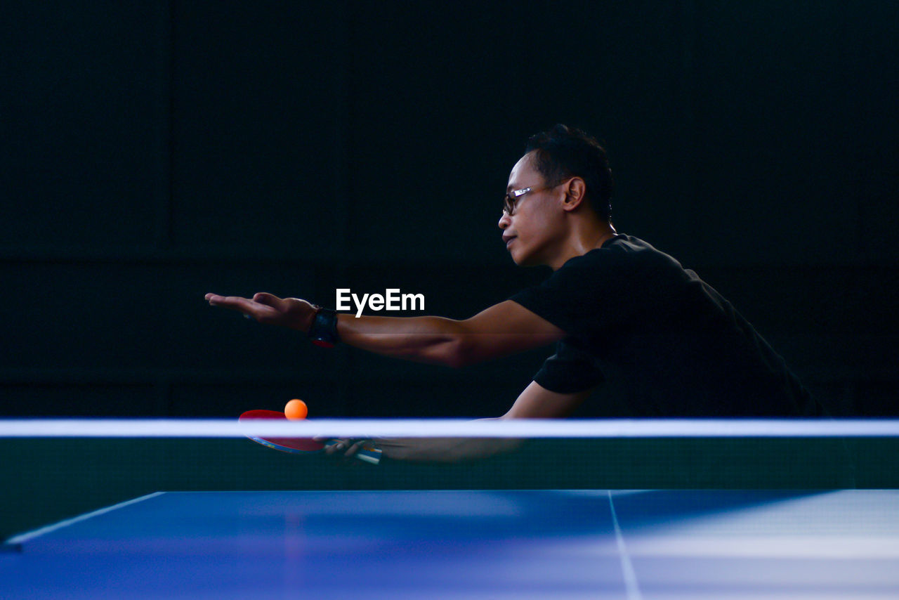 Young man playing table tennis in dark