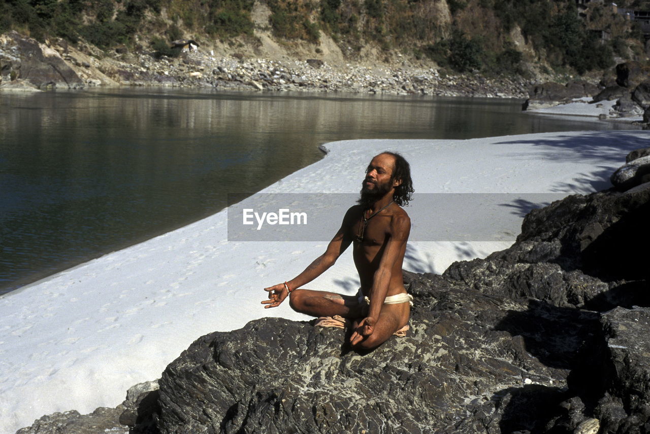 Man meditating on rock by frozen lake