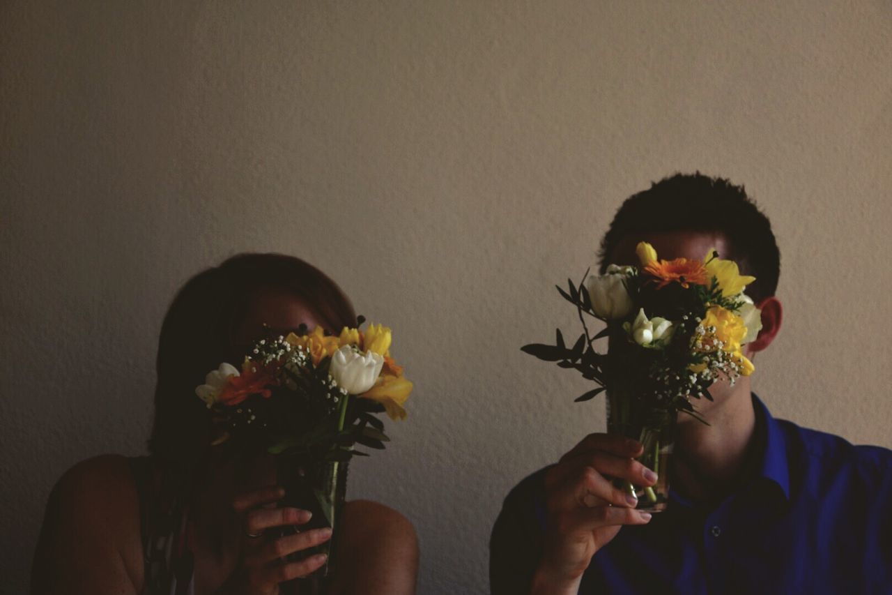 Obscured friends faces from flowers against wall