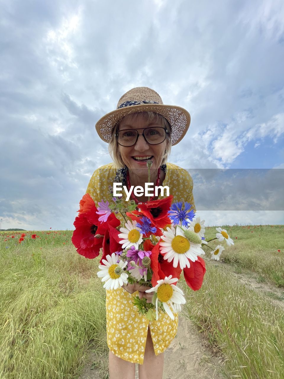 Portrait of a radiant woman with a summer hat and a colorful bouquet of flowers in a meadow