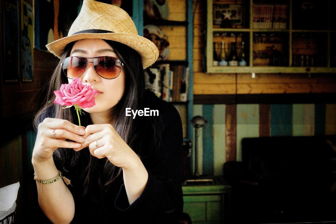Portrait of woman in sunglasses and hat holding flower at home