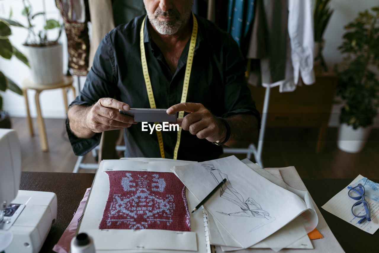 Talented male tailor photographing patterned fabric at work studio