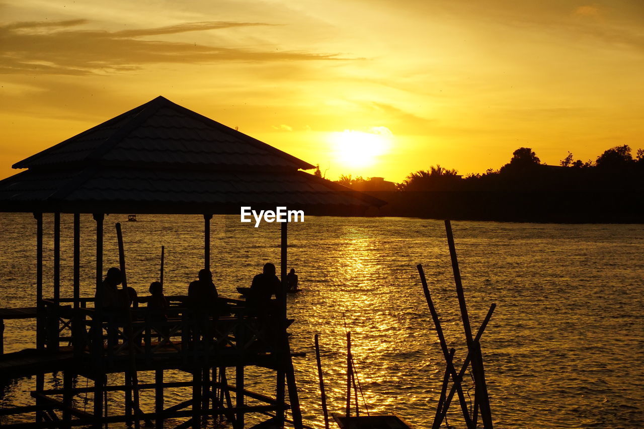 Silhouette built structure by river against sky during sunset