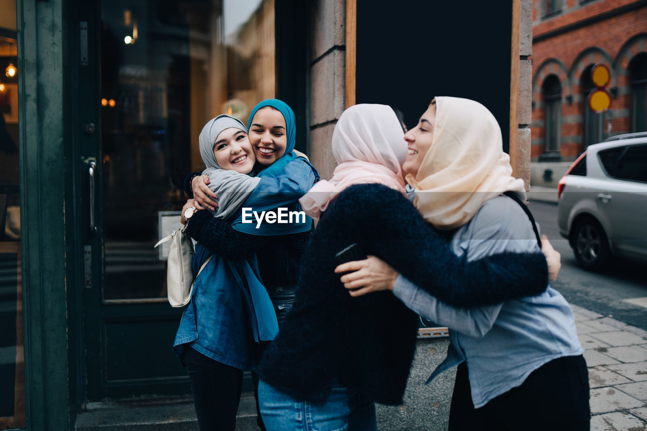 Smiling multi-ethnic female friends greeting on sidewalk in city