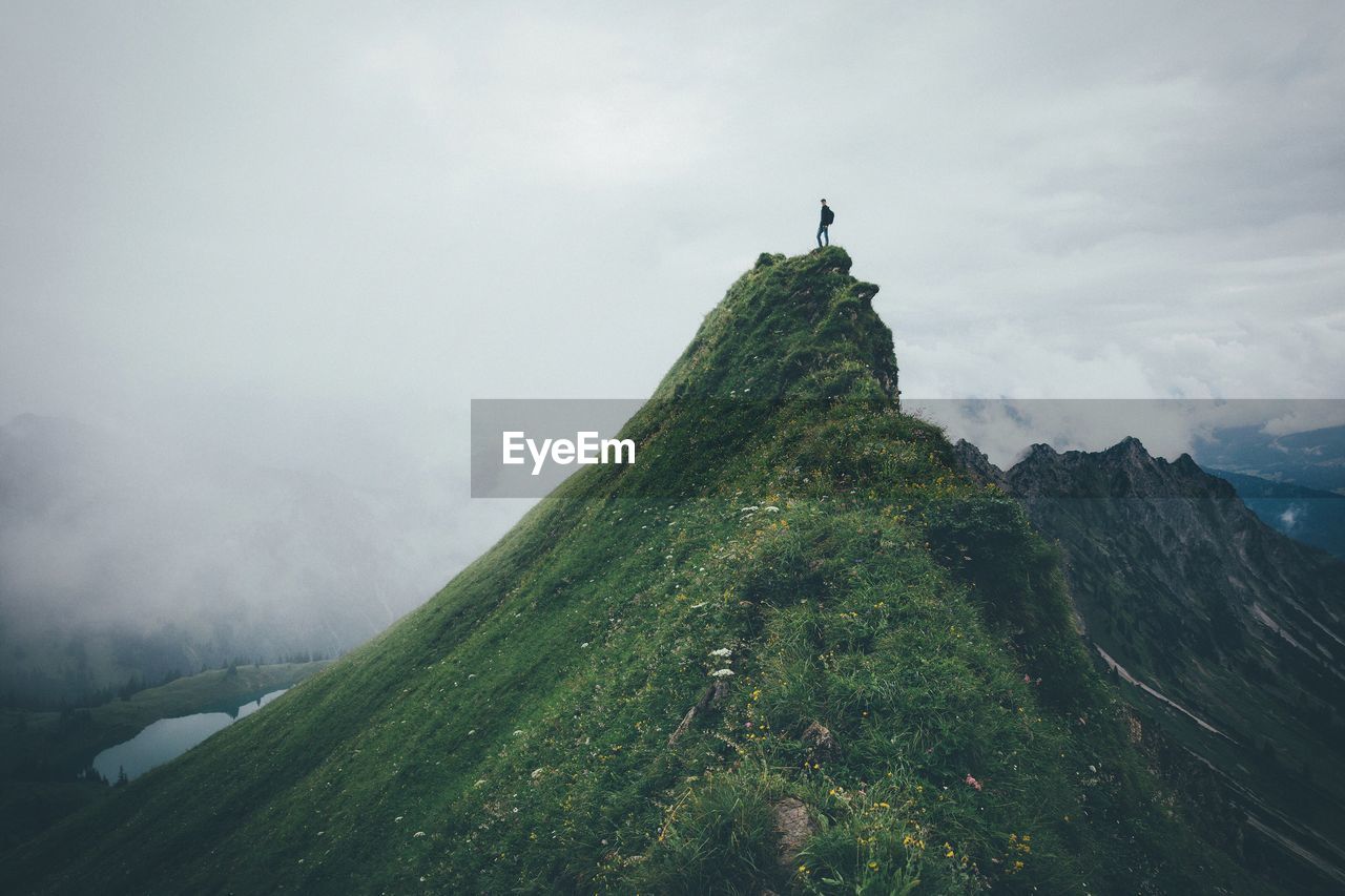 Man standing on mountain peak against cloudy sky