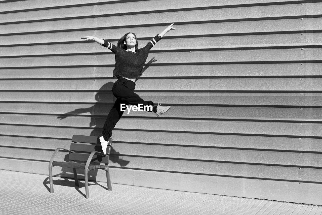 Woman jumping from chair by wall