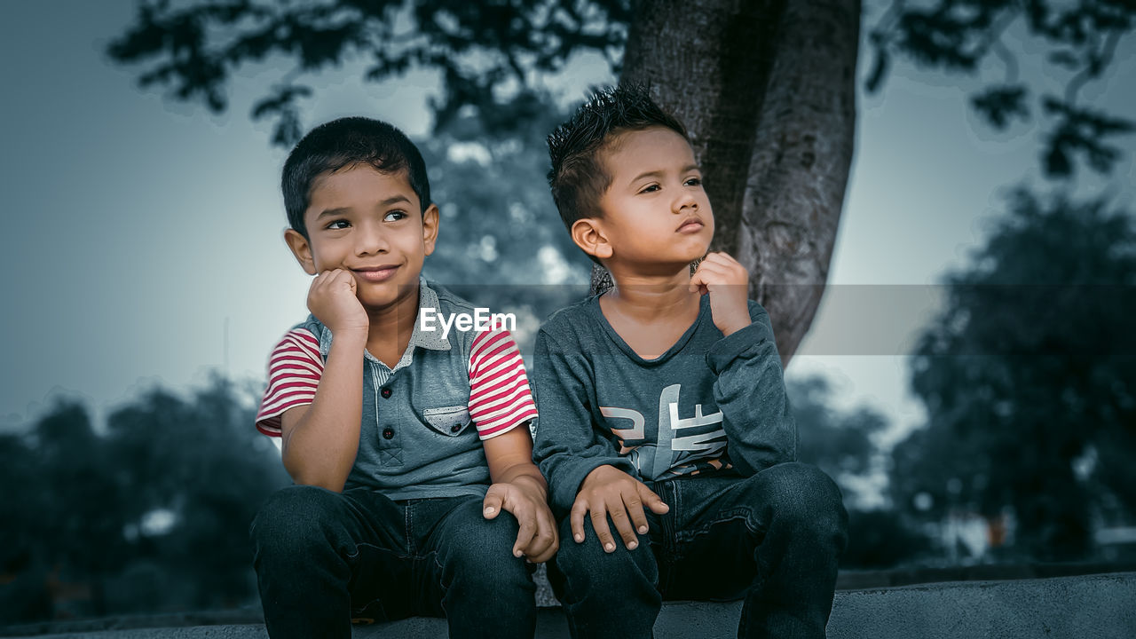 Happy friends sitting against trees
